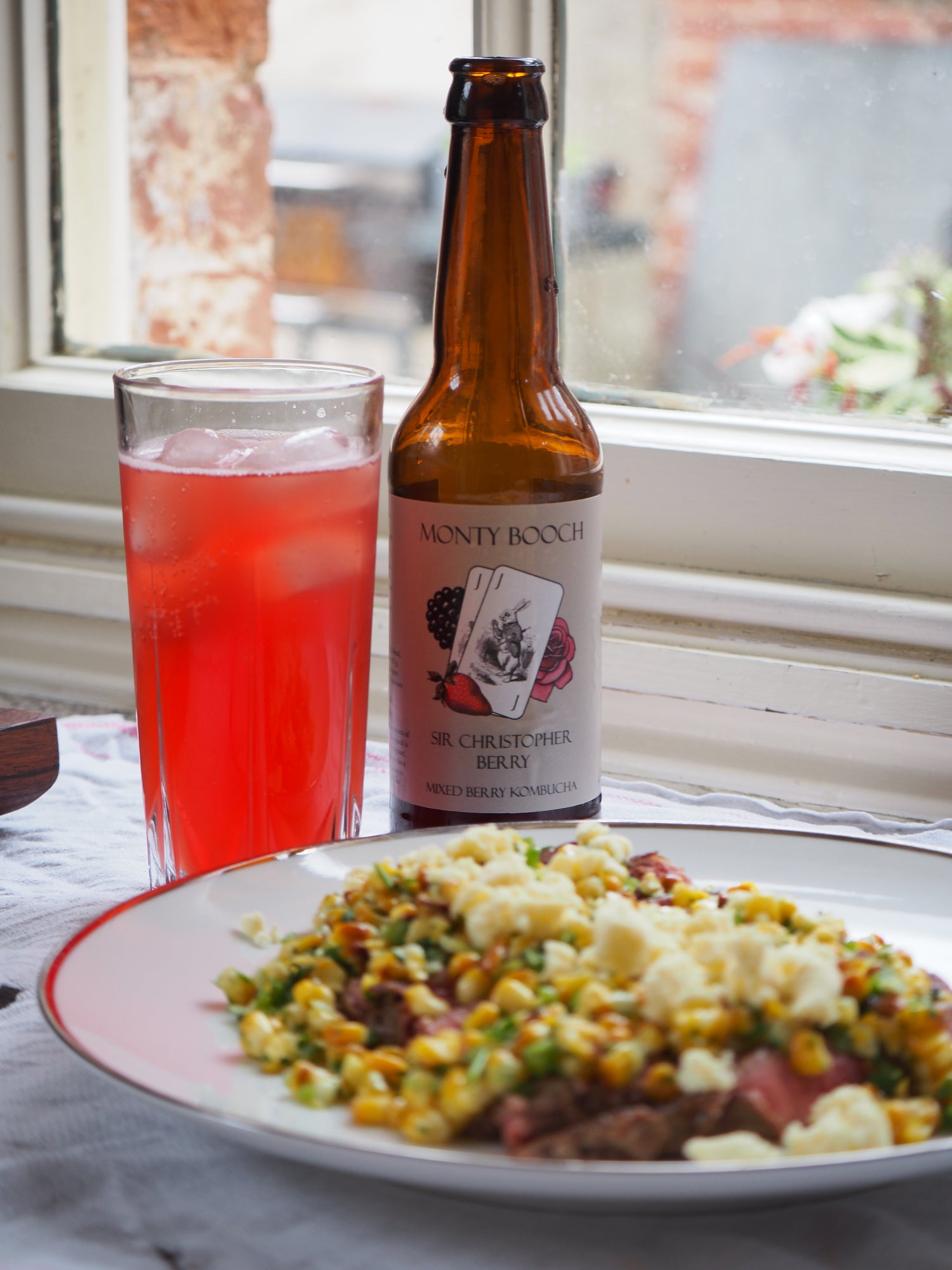 Bottle of monty booch kombucha on a table with a dish of food in the foreground.